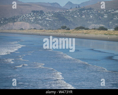 New Brighton, New Zealand, beach with distant mountains, gentle waves and silhouette of people walking Stock Photo