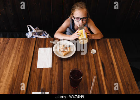 Little girl eats and drinks at table in cafe restaurant