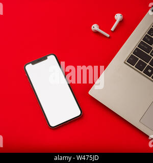 Tula, Russia - May 24,2019: Apple iPhone X and Airpods on red background with notebook. The screen of the smartphone is white. Mockup. Stock Photo