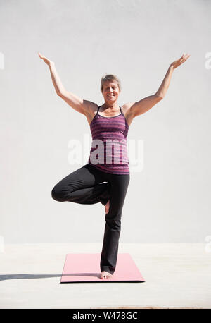 Middle aged women practicing yoga in Lotus pose or Padmasana with raised  hands namaste behind the back. Meditation with yoga in white bedroom after  wake up in the morning. 21160414 Stock Photo