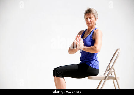 Senior woman in a prayer pose doing yoga with hands behind her