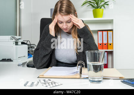 a woman in the office with headaches leans on the table Stock Photo