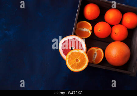 Fresh sliced oranges and grapefruit on wooden basket on vibrant blue background. Stock Photo