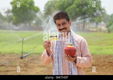 Farmer showing credit card and holding a piggy bank Stock Photo