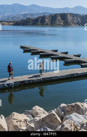 A couple walk out along the Wood boat dock / jetty at Lake Cachuma to rent a boat and spend a day fishing.Santa Barbara County, California ; USA Stock Photo