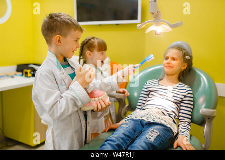 Children in uniform playing dentist doctor, playroom. Kids plays medicine worker in imaginary hospital, stomatologist profession learning, childish dr Stock Photo