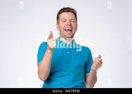 Handsome young man laughing at joke with folded hands. Studio shot Stock Photo