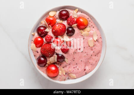 smoothie bowl or nice cream made of frozen bananas and berries with fresh berries, nuts and seeds on white marble table. healthy breakfast. top view
