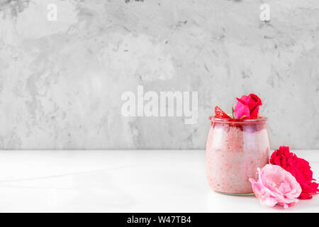 overnight oats with fresh strawberries in a glass with rose flowers on white marble table. healthy diet breakfast with copy space Stock Photo