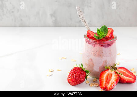 overnight oats with fresh strawberries and mint in a glass on white marble table. healthy diet breakfast. close up Stock Photo
