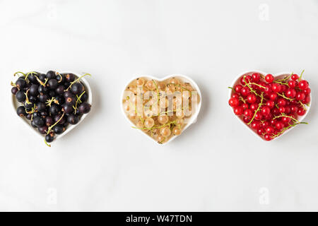variety of currant berries black, red and white in heart shape bowls on white marble background. summer food concept. flat lay. top view Stock Photo