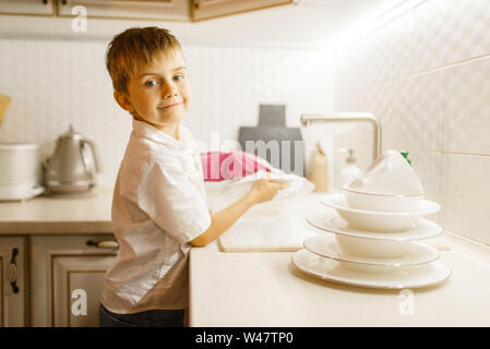 A little boy in gloves washing dishes on the kitchen. Baby doing housework at home. Young mom's helper clean the house Stock Photo
