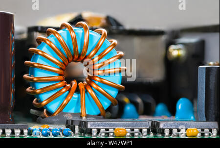 Blue coil core with copper wire winding on integrated circuits. Toroidal inductor detail and microchips. Electronic components on PCB. Electrotechnics. Stock Photo