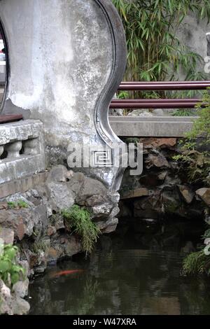 Asian garden in Shanghai, China. Footbridge with railing and ornate grey concrete or stone balustrade and railing above a tranquil, still stream with Stock Photo
