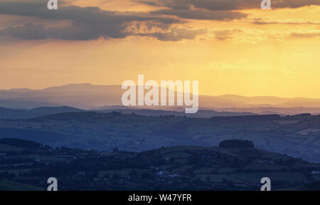 Warm yellow sunset light over rolling peaks of farming fields in Shropshire, United Kingdom Stock Photo