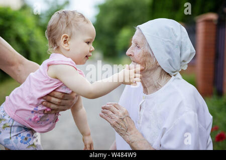 Cute toddler girl playing with her great grandmother and touching her face outdoors Stock Photo