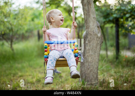 Laughing little girl on swing in summer garden Stock Photo