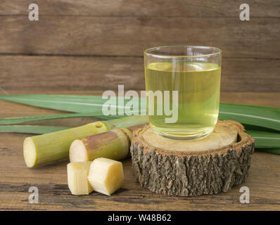 Freshly squeezed sugar cane juice in glass with cut pieces cane on a wooden table. Stock Photo