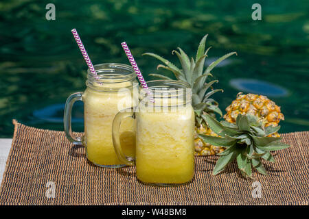 Homemade mango and pineapple smoothie made with coconut milk in two glass mug near swimming pool, close up. Island Bali, Indonesia. Refreshing tropica Stock Photo