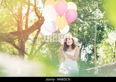 Beautiful young woman holding air balloons in garden Stock Photo