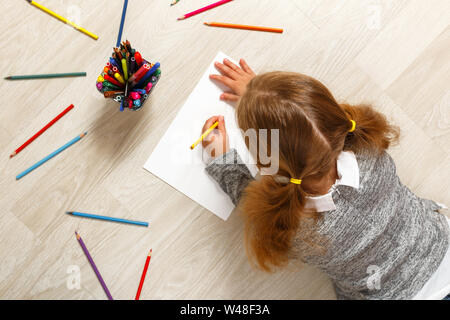 Top view of a little girl lying and painting on the floor in her room at home. Stock Photo