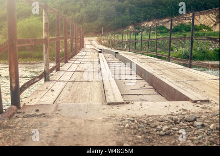 Low Angle Perspective View of the Old Bridge over the Mountain River with Steel Beams, Wooden Boards. Evening Sun Flare. Stock Photo