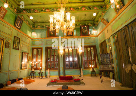 aipur, Rajasthan, India - circa 2017: Green walled room with a chandelier, lights and ground seating for royalty in Udaipur city palace. These old maj Stock Photo