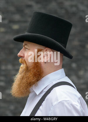 Side view Portrait of a bearded man in retro style fashion wearing braces and a black top hat Stock Photo