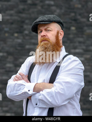 Portrait of a overweight bearded man in cloth hat and braces standing with folded arms Stock Photo
