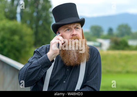 Thoughtful man in old fashioned top hat and braces leaning on a bridge railing chatting on his mobile Stock Photo