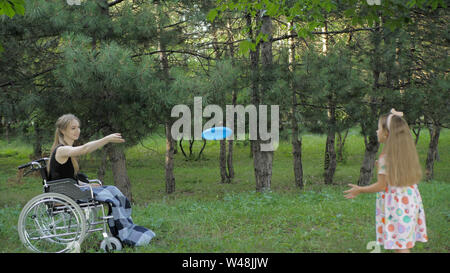 Beautiful blonde girl is sitting in wheelchair and having fun by playing with the flying disc. Stock Photo