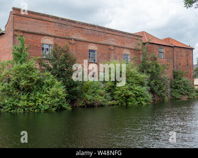 A derelict red brick building on the banks of the river Wensum in Notwich, with foliage growing on it Stock Photo