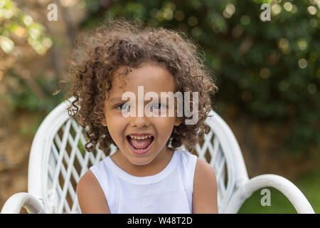 A head and shoulders portrait of smiling toddler boy with curly hair shot outdoors with natural light. A head and shoulders portrait of smiling toddler boy with curly hair shot outdoors with natural light.