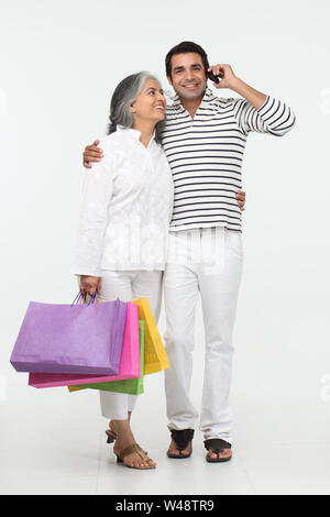 Senior woman carrying shopping bags with her son talking on mobile phone Stock Photo