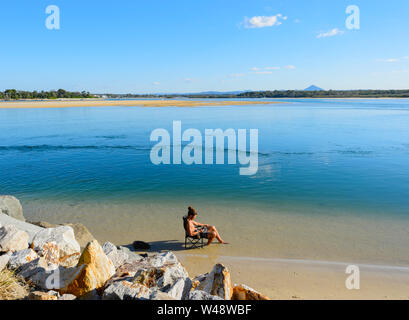 Man with a man bun relaxing on a chair in the water at Noosa Main Beach, Noosa Heads, Sunshine Coast, Queensland, QLD, Australia Stock Photo