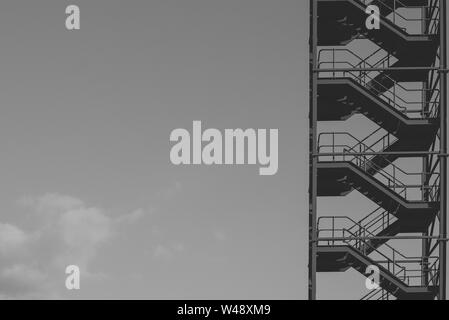 Black and white photo of an industrial ladder contrasting with a cloudy sky in the background. Stock Photo