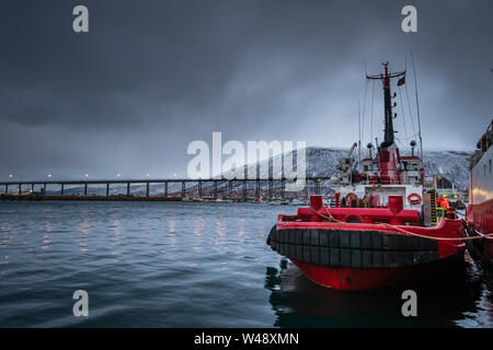 Tromso, Norway -  December 2018 : Fishing boat in port and harbour in Tromso, with famous Tromso Bridge across Tromsoysundet strait in the background Stock Photo