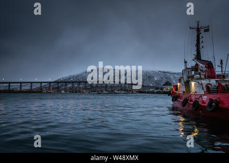 Tromso, Norway -  December 2018 : Fishing boat in port and harbour in Tromso, with famous Tromso Bridge across Tromsoysundet strait in the background Stock Photo