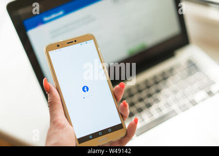 Kedainiai, Lithuania - June 25, 2019: woman hand holding Huawei smartphone with Facebook app on background of Macbook with Facebook main login page on Stock Photo
