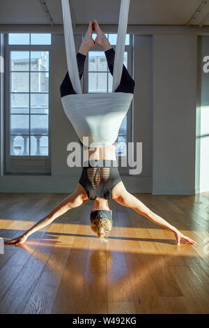 Beautiful girl aerial yoga trainer shows medutiruet on hanging lines upside down in a yoga room. Concept yoga, flexible body, healthy lifestyle Stock Photo