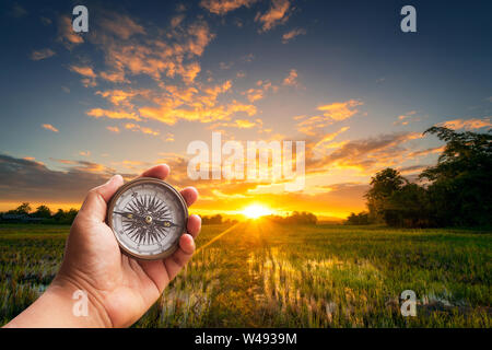 A man holding compass on hand at field and sunset for navigation guide. Stock Photo
