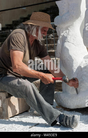 Senior sculptor working outdoor on his marble sculpture in his workshop with hammer and chisel Stock Photo