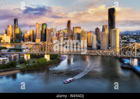 CLose to Story bridge across Brisbane river in front of Brisbane city CBD high-rise business and apartment towers with fast ferry on the water under t Stock Photo
