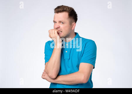 Young caucasian man in blue shirt biting nails being stressed or nervous. Stock Photo