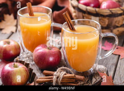 Two cups of apple cider and cinnamon sticks with fresh red apples on a rustic wooden surface Stock Photo