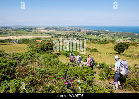 Hikers hiking down a footpath on Mynydd Eilian with view to Amlwch on the coast. Llaneilian, Isle of Anglesey, north Wales, UK, Britain Stock Photo
