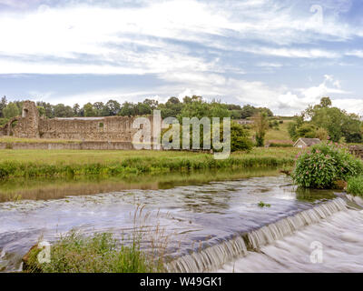 Water from the River Derwent rushes down a weir and the ruins of an ancient abbey are on the far bank. A cloudy sky is above. Stock Photo
