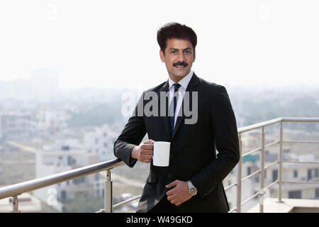Businessman standing by a railing and having a cup of coffee Stock Photo