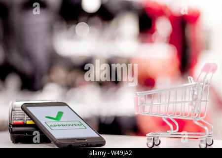 POS terminal, Payment Machine with mobile phone on store background. Contactless payment with NFC technology. Stock Photo