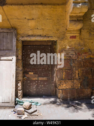 Broken wooden brown door on grunge stone bricks wall painted in orange in abandoned Darb El Labana district, Cairo, Egypt Stock Photo